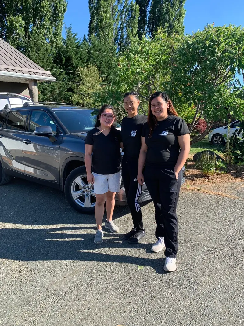 Three Crystal Care cleaners in uniform smiling in a sunny driveway beside their car